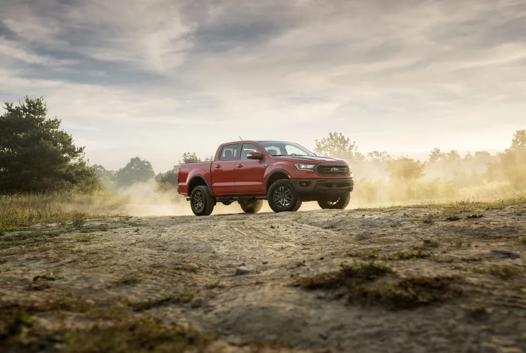 A 2021 Ford Ranger pick up truck in red parked on a dirt road with dust rolling up behind it.