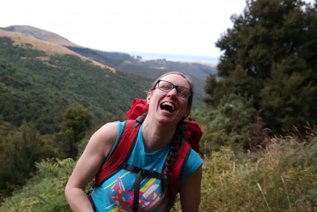 Woman throwing her head back in laughter while on a hike in the woods.