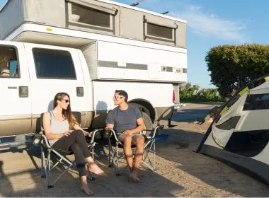 A couple sitting outside a pop up truck camper.