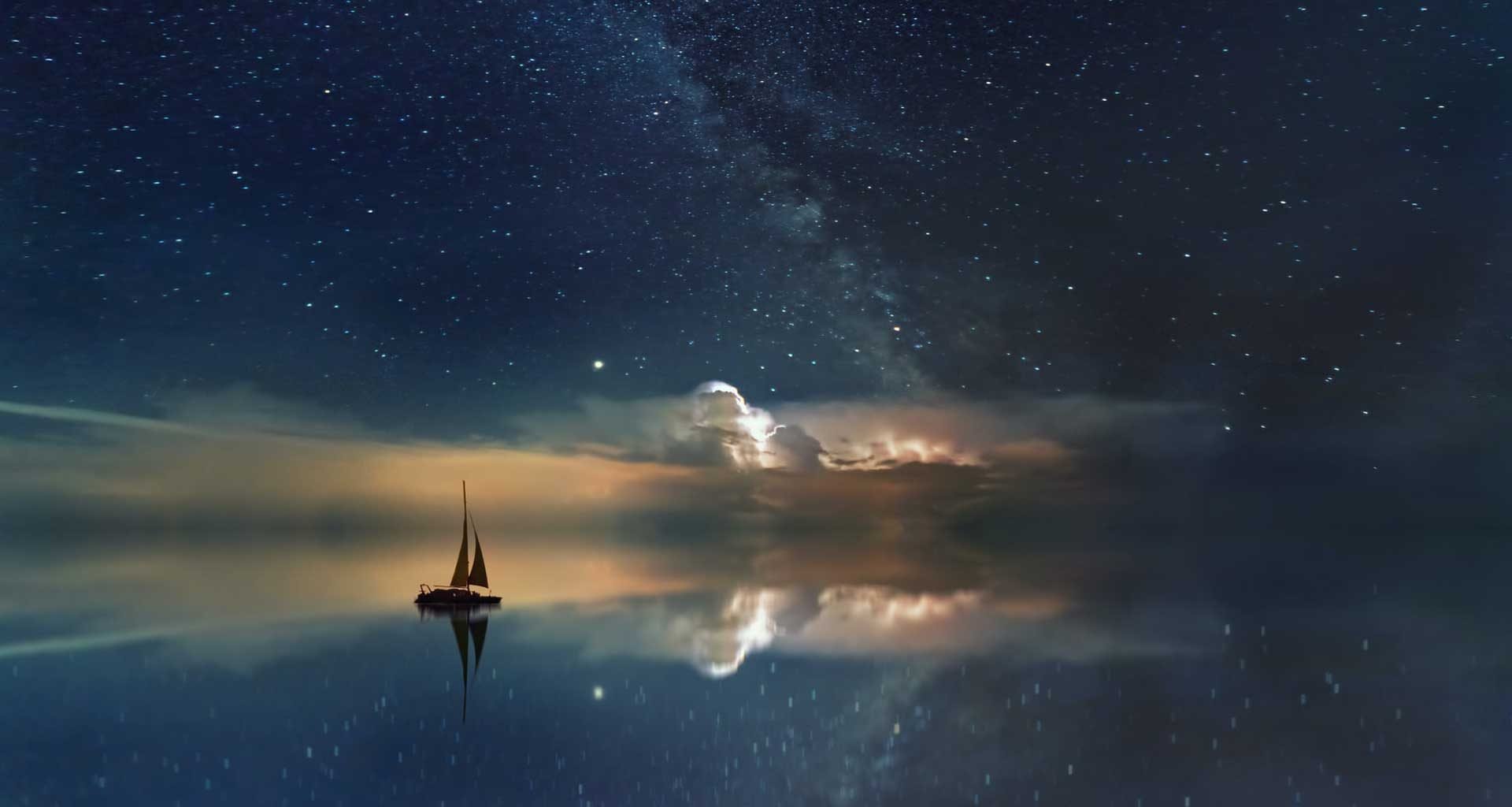 A lone sailboat out in the ocean at night.