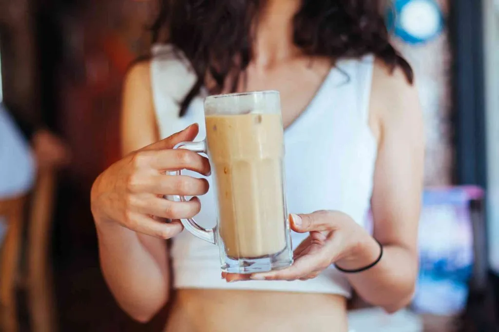 A young woman in a crop top holds a glass filled with diet coke and coffee creamer.